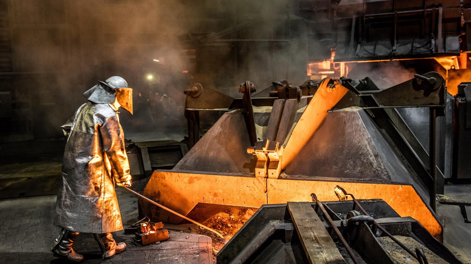 Ein Mitarbeiter der Salzgitter AG steht in Schutzkleidung vor einem Hochofen und entnimmt eine Roheisenprobe. | Salzgitter AG