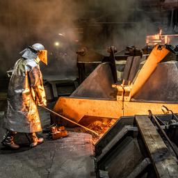 Ein Mitarbeiter der Salzgitter AG steht in Schutzkleidung vor einem Hochofen und entnimmt eine Roheisenprobe.