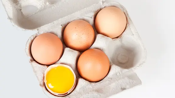 Eier sind eine wichtige Zutat für eine Vielzahl von Gerichten. | Fotolia, Bernd Kröger Ein Karton mit vier ganzen Eiern und einer Eischale mit Eigelb.