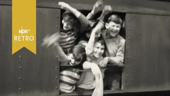 Fünf Kinder winken zum Abschied aus dem Fenster eines abfahrenden Zugwaggons (1959)