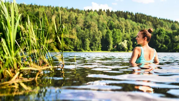 Eine Frau badet in Ufernähe in einem See.