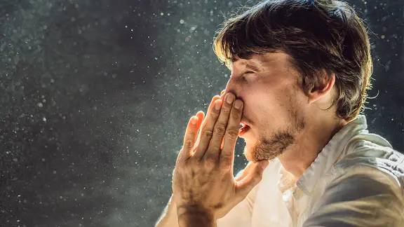 Ein Mann niest in die Hände, im Gegenlicht sind Staubkörner in der Luft zu sehen. | Panthermedia, Panthermedia | galitskaya Ein Mann niest in die Hände, im Gegenlicht sind Staubkörner in der Luft zu sehen.