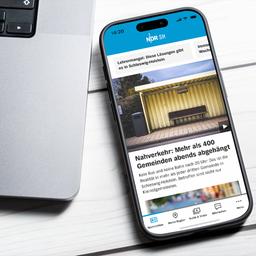 Ein Smartphone auf dem die NDR SH App zu sehen ist, liegt auf dem Tisch neben einem Laptop.