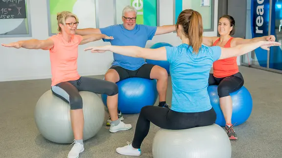 Eine Rehasport-Gruppe macht unter Anleitung Übungen mit dem Gymnastikball.