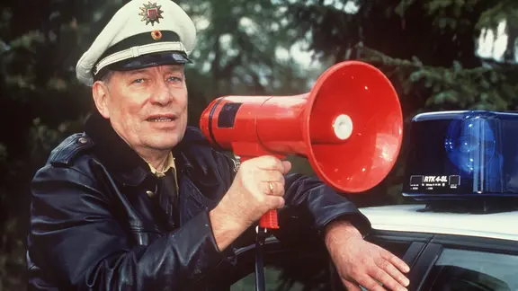 Jürgen Roland in Polizeiuniform mit einem roten Megafon in der Hand.