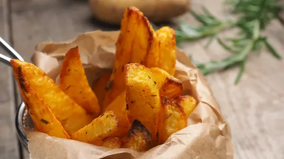 Wedges eignen sich besonders gut für die Zubereitung im Ofen. | Colourbox, Andreas Berheide Kartoffel-Wedges in einem mit Backpapier ausgelegtem Sieb.