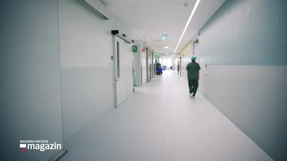 Eine Person in grüner OP-Kleidung geht einen Klinik-Flur entlang.