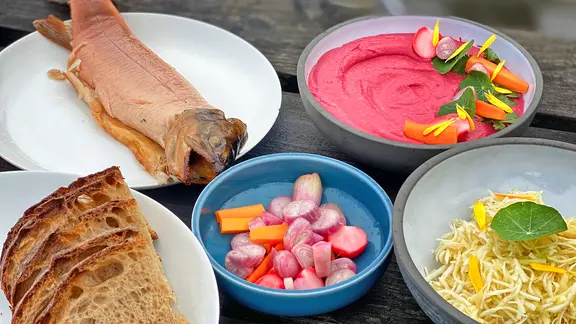 Fisch, Brot, Dip und Salate in verschiedenen Tellern und Schälchen angerichtet 