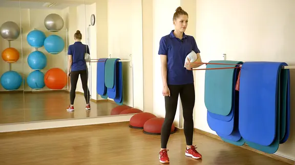 Svea Köhlmoos klemmt ein Kissen unter den Arm und zieht dabei am Theraband.