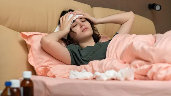 Kranke Frau liegt im Bett und hält sich schmerzenden Kopf (Bild: colourbox.de/Erstudio)