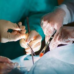 Hände mit medizinischen Geräten an einem OP-Tisch.