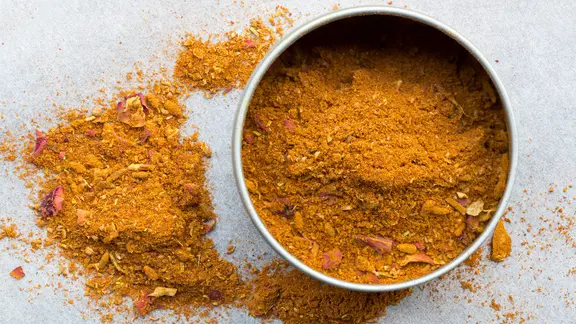 Die Gewürzmischung Ras el hanout in einer Dose und auf einer Arbeitsfläche verstreut.