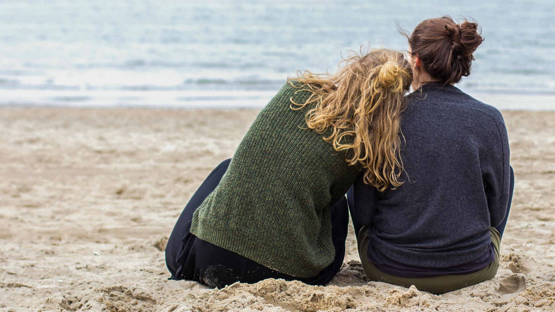 Zwei Frauen sitzen nebeneinander am Strand und schauen aufs Meer. | photocase , thesunny