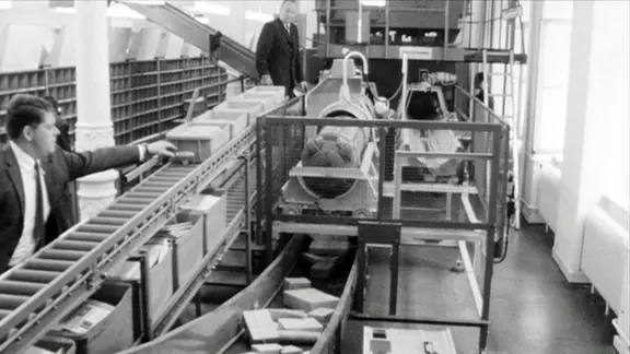 Zwei Männer an Förderbänder neben einer Rohrpostanlage