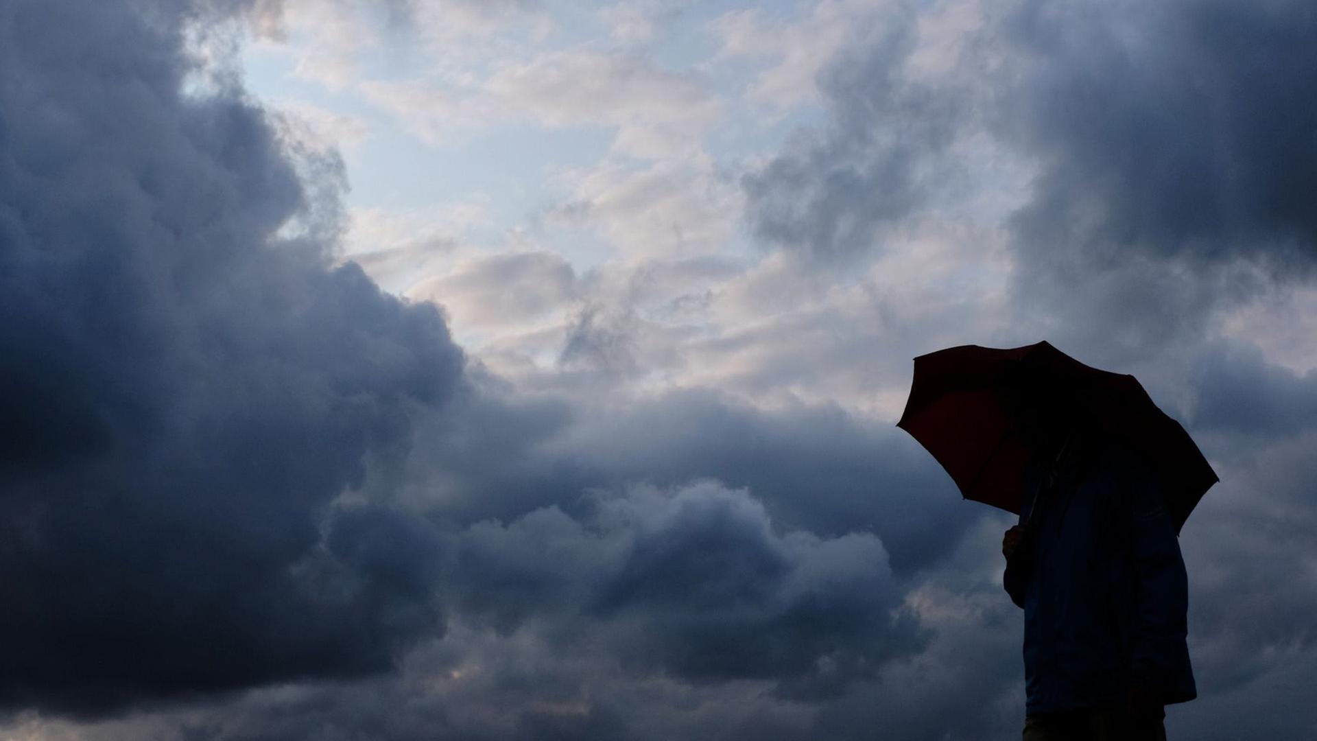 Ein Mann geht mit einem Regenschirm vor aufziehenden dunklen Wolken spazieren.  | Martin Gerten, dpa