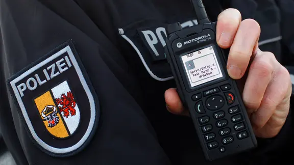 Ein Polizist hält ein Funkgerät.