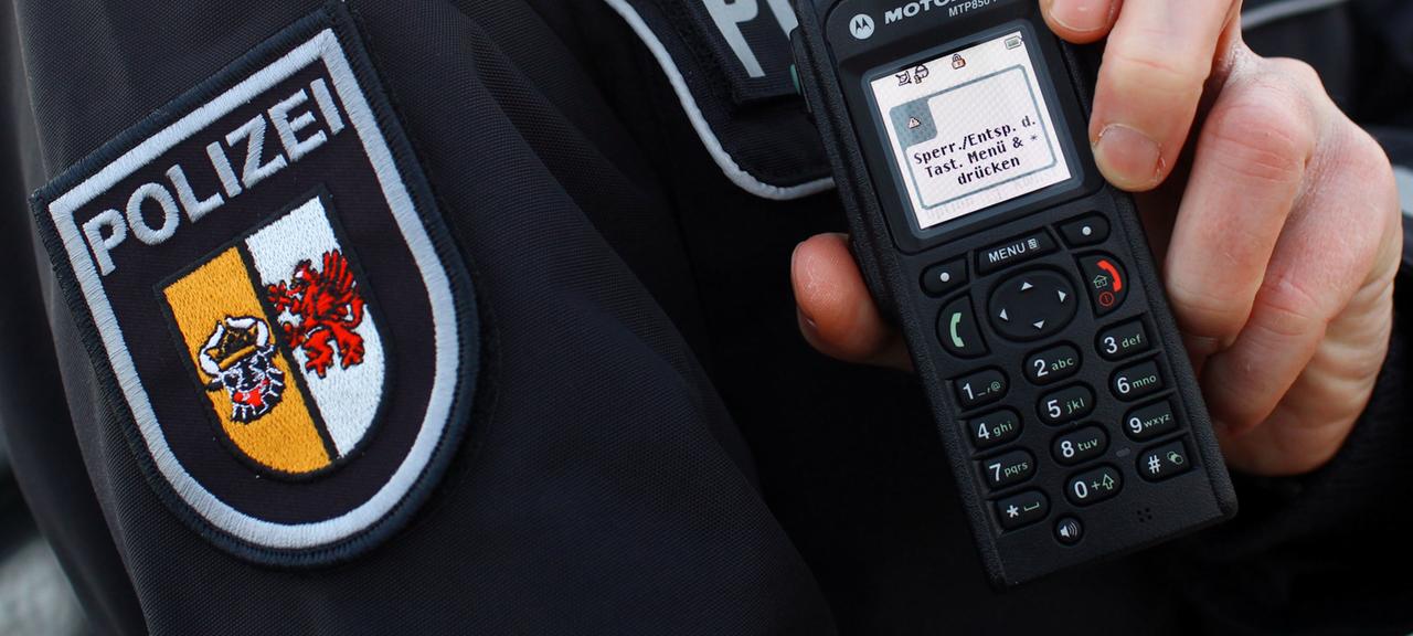 Ein Polizist hält ein Funkgerät.