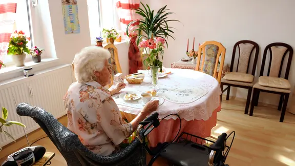 Seniorin sitzt an ihrem Esstisch bei Kaffee und Kuchen