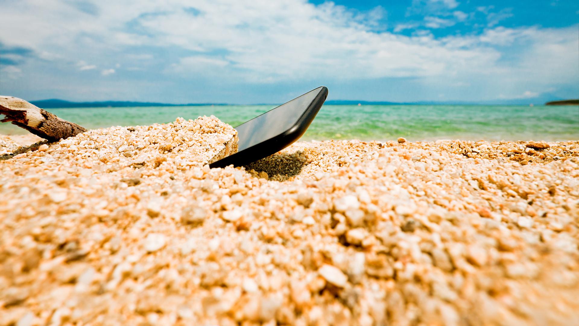 Ein Smartphone ist am Strand in den Sand gefallen. | Colourbox, -