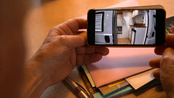 Auf einem Handy wird ein Video gezeigt von einem ausgebauten Wohnmobil.
