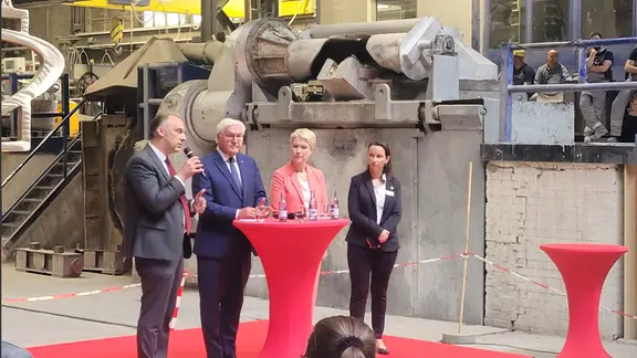 Unter anderem Bundespräsident Frank-Walter Steinmeier und Ministerpräsidentin Manuela Schwesig stehen auf einem Podes in einer Werkhalle in Waren.