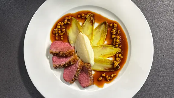 Barbarie-Entenbrust mit Chicorée und Topinamburpüree auf einem weißen Teller angerichtet