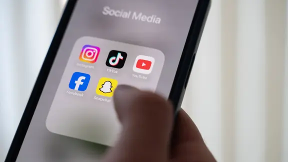 Eine Person hält ein Smartphone, auf dessen Display verschiedene Social Media Apps angezeigt werden.