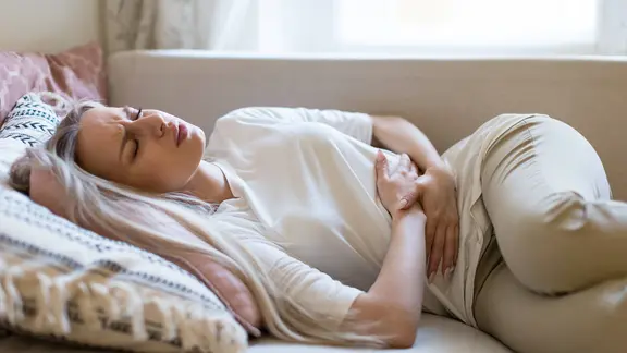 Frau liegt mit Bauchschmerzen auf dem Sofa