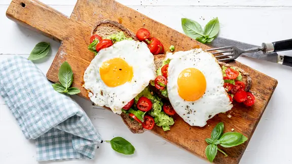 Zwei Spiegeleier auf einer Scheibe Brot auf einem Holzbrett. | ZS-Verlag, Claudia Timmann Zwei Spiegeleier auf einer Scheibe Brot auf einem Holzbrett.