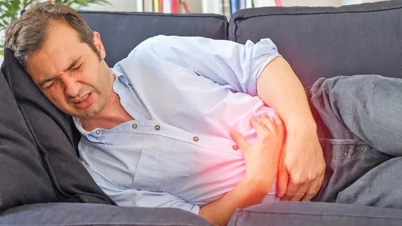 Ein Mann liegt mit Magenschmerzen auf dem Sofa.