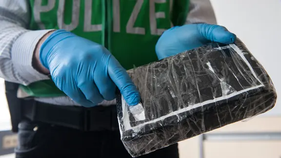 Ein Polizeibeamter öffnet ein Drogenpaket mit weißem Pulver.