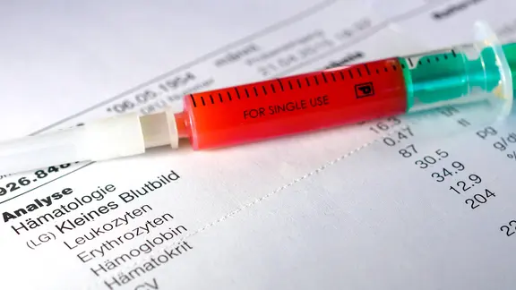 Blutwerte: Kanüle mit Blut liegt auf Zettel mit Laborwerten
