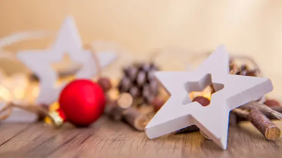 Ein hölzerner Stern, eine Christbaumkugel und weitere Dekoration liegen auf einem hölzernen Untergrund.