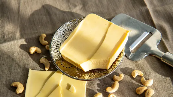 Veganer Käse liegt auf einem kleinen Teller, daneben befinden sich abgeschnittene Scheiben und Cashewnüsse.