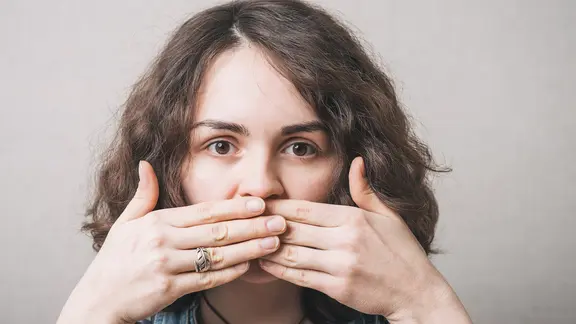 Frau blickt in die Kamera und hält sich dabei Hände vor den Mund (Bild: colourbox.de) | colourbox.de Frau blickt in die Kamera und hält sich dabei Hände vor den Mund (Bild: colourbox.de)