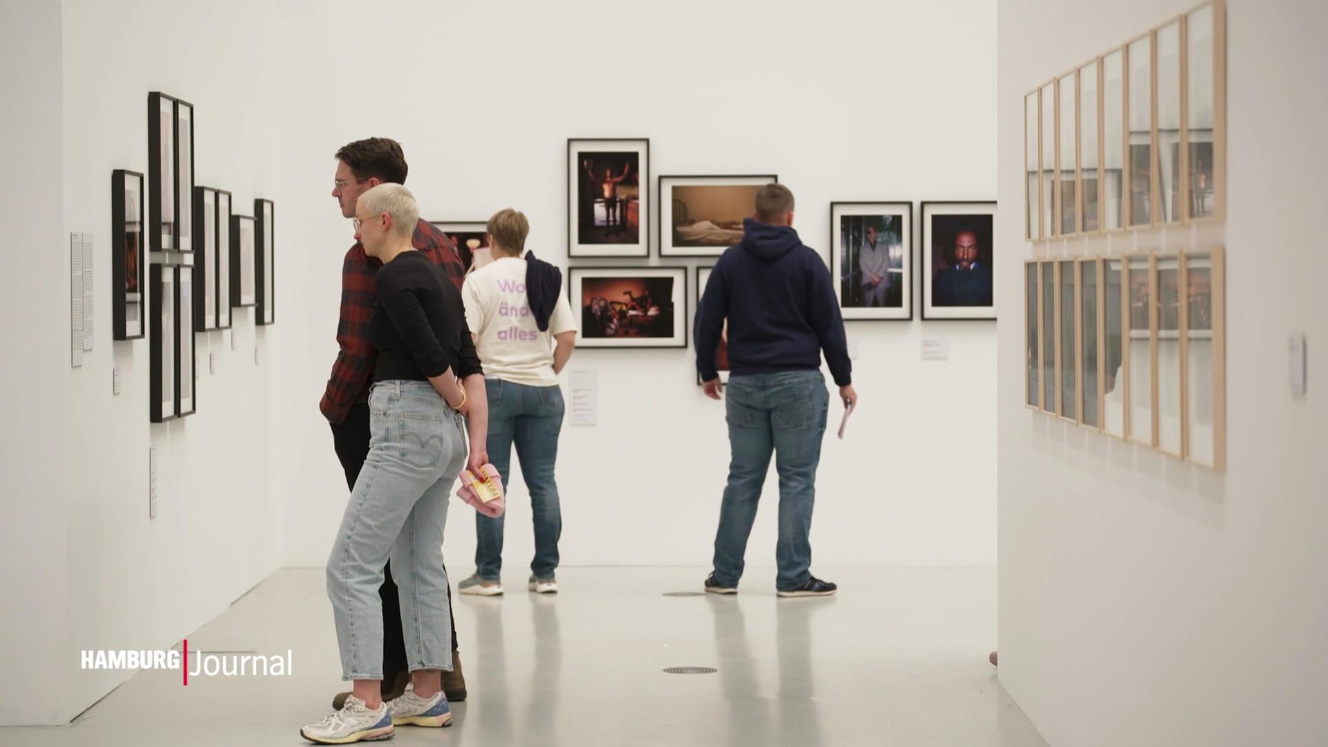 Mehrere Personen stehen in einer Ausstellung. | Screenshot