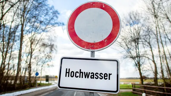 Ein Schild mit der Aufschrift "Hochwasser" steht vor einer gesperrten Straße in Sandkrug.
