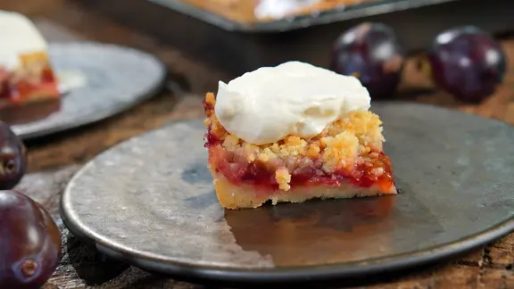 Ein Stück Zwetschgenkuchen mit Streuseln auf einem dunklen Teller