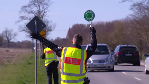 Ein Polizist ist von hinten zu sehen, wie er ein Fahrzeug rauszieht.