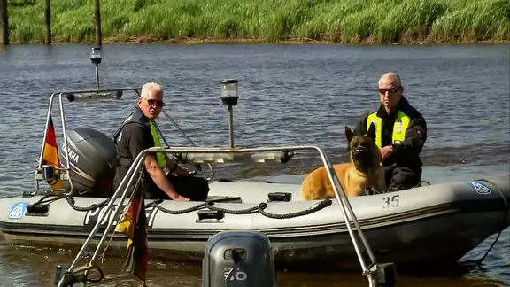 Zwei Polizisten fahren mit einem Polizeihund auf einem Boot über die Oste.