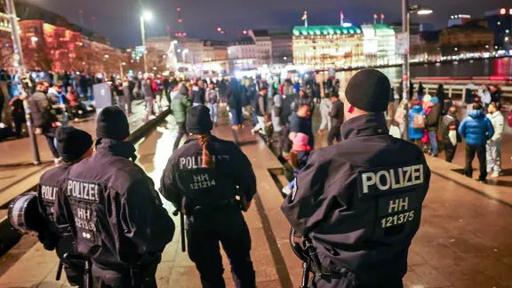 Polizistinnen und Polizisten stehen im Dunkeln am Jungfernstieg und beobachten viele Menschen, die zusammen feiern.