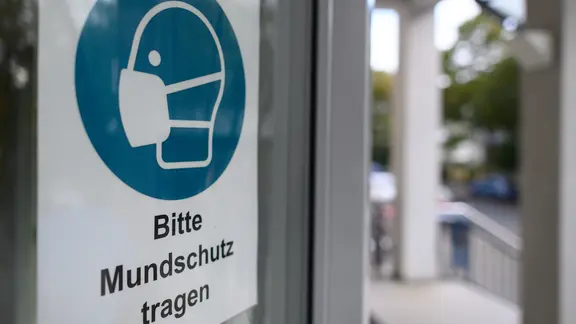 Ein Schild "Bitte Mundschutz tragen" ist am Eingang eines Krankenhauses angebracht.