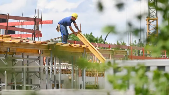 Ein Bauarbeiter nimmt auf einer Baustelle einen Balken entgegen. (Symbolfoto)