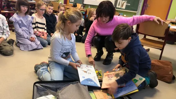 Kinder sitzen auf dem Fußboden und schauen sich mehrere Bücher an.