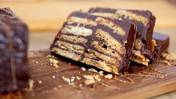 Ein aufgeschnittener Kekskuchen mit Schokolade (Kalter Hund) liegt auf einem Holzbrett. | NDR, Claudia Timmann Ein aufgeschnittener Kekskuchen mit Schokolade (Kalter Hund) liegt auf einem Holzbrett.