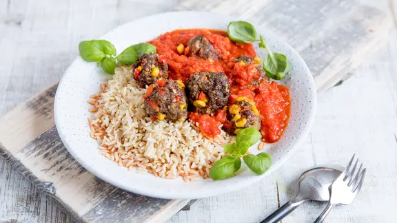 Ein Teller mit Reis und Hackbällchen in Tomatensoße steht auf dem Tisch.