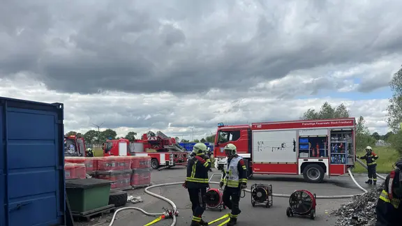 Feuerwehrleute mit ausgelegten Schläuchen mit Feuerwehrautos im Hintergrund