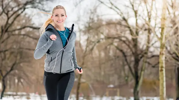Eine junge Frau joggt durch eine Winterlandschaft.