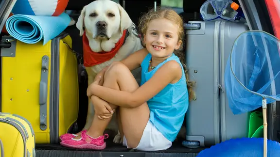 Ein Mädchen und ein Hund sitzen in einem voll gepackten Kofferraum