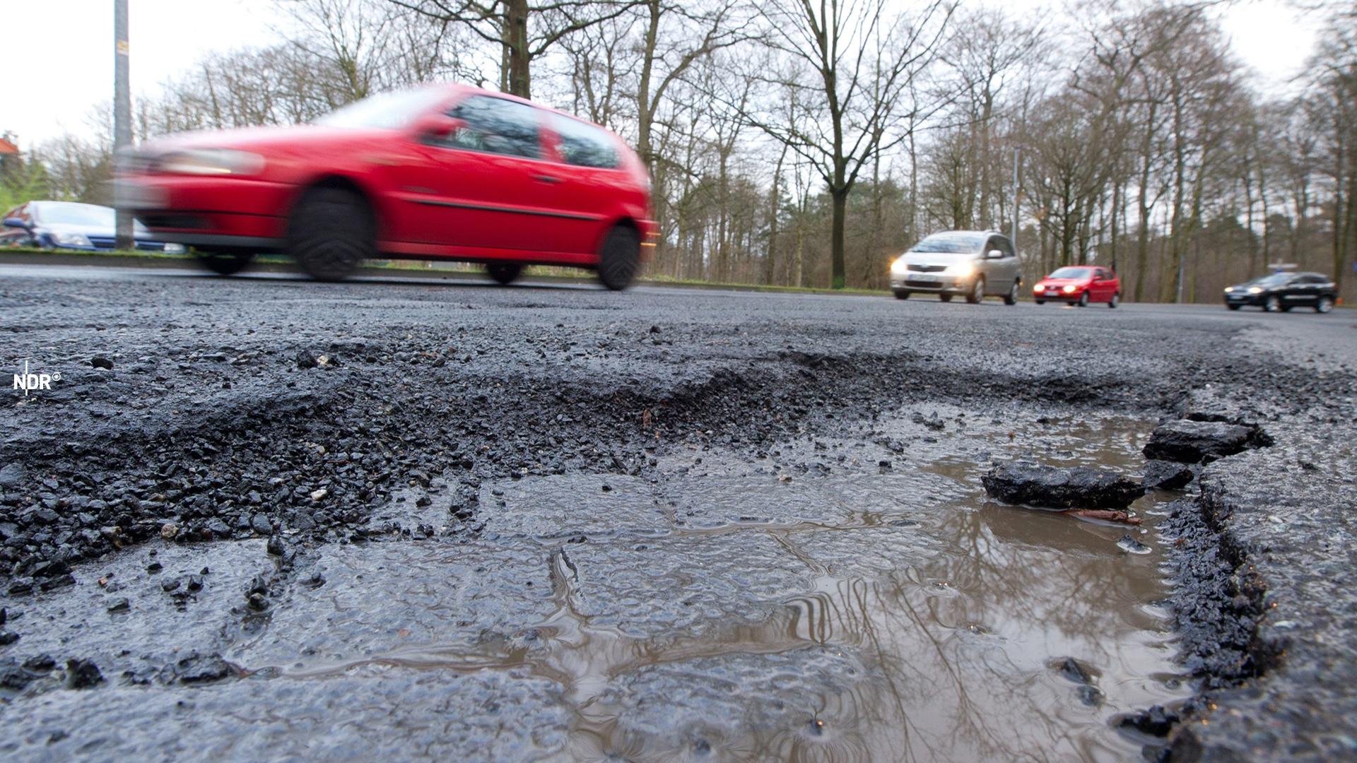 Autos fahren an einem Schlagloch auf einer Straße vorbei.